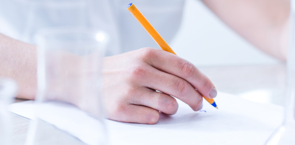 Close-up of student writing report during chemistry lesson