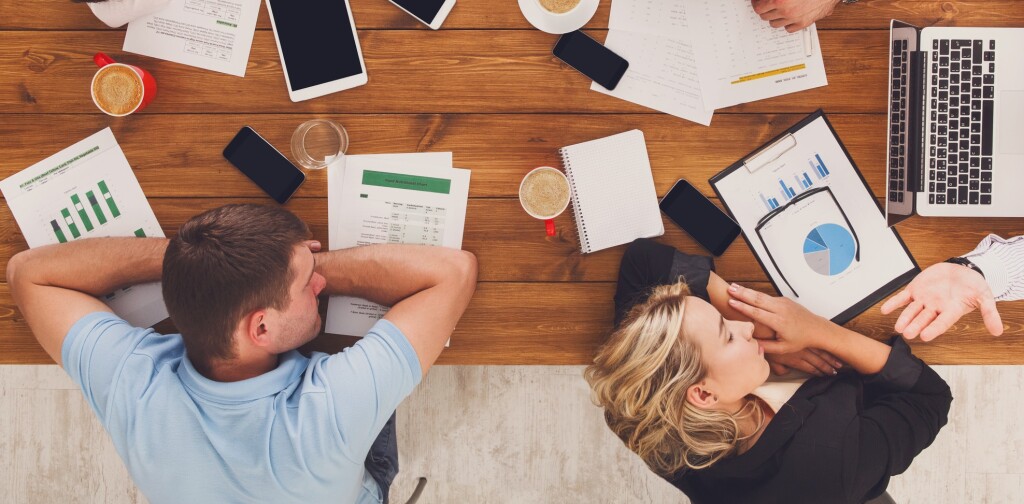 Group of business people exhausted sleep in office, top view of wooden table with mobile phones, laptop, tablet and papers with diagram. Men and women team tired and relaxed after brainstorm