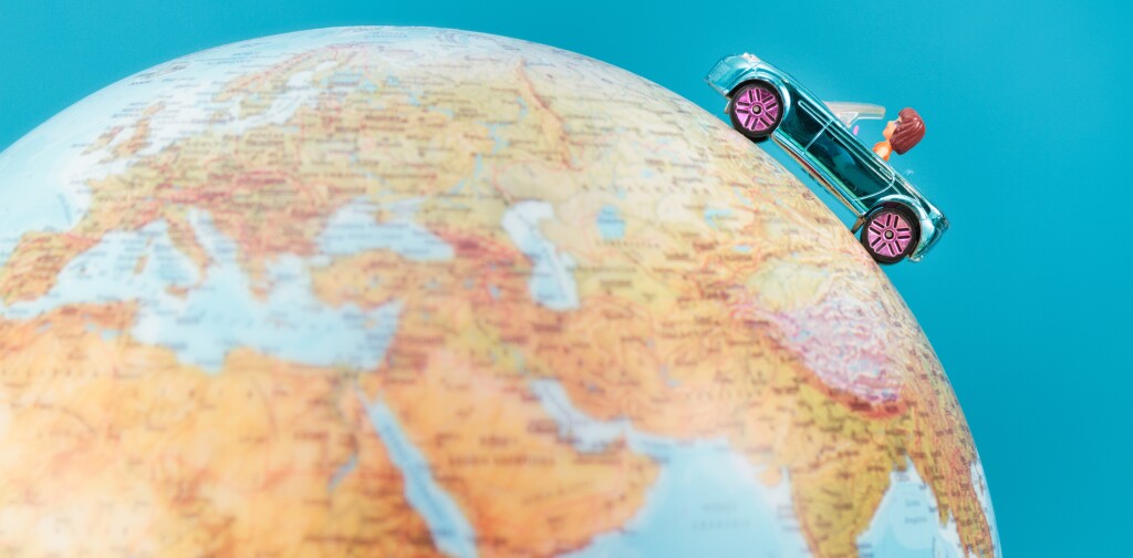 Toy car on the globe on plain blue background. Space for text
