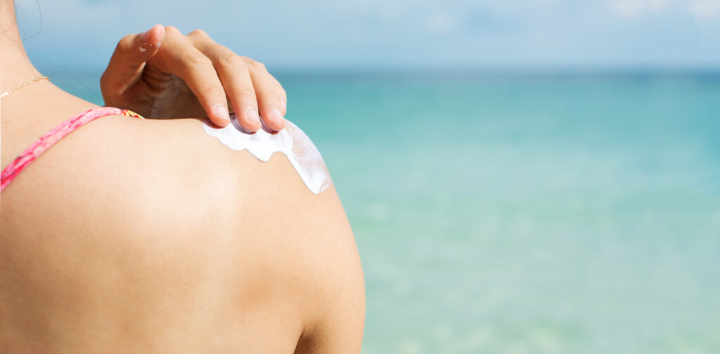 Girl applying sun lotion on the beach back view