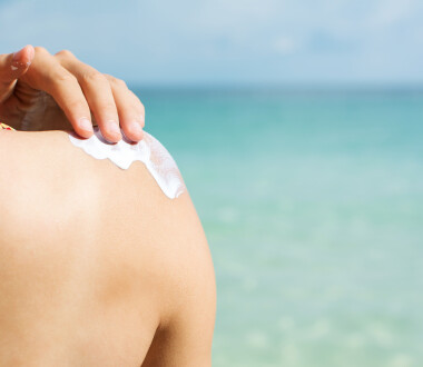 Girl applying sun lotion on the beach back view
