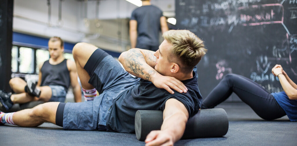 Man rolling on foam roller at health club. Male athlete exercising in gym. He is in sports clothing.