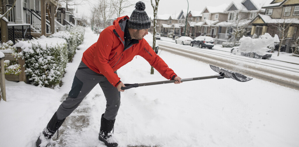 Side view shot of man shoveling snow off sidewalk in winter in suburb