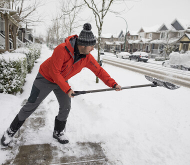 Side view shot of man shoveling snow off sidewalk in winter in suburb