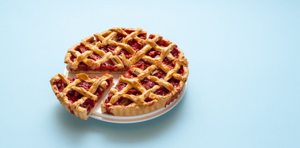 Rhubarb and strawberry pie sliced in portions, isolated on a blue seamless background. German rhubarb cake. Handmade sweet pie on white plate.