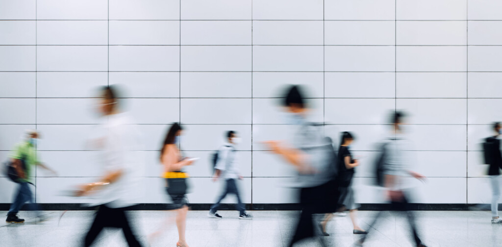 Blurred motion of a crowd of busy commuters with protective face mask walking through platforms at subway station during office peak hours in the city