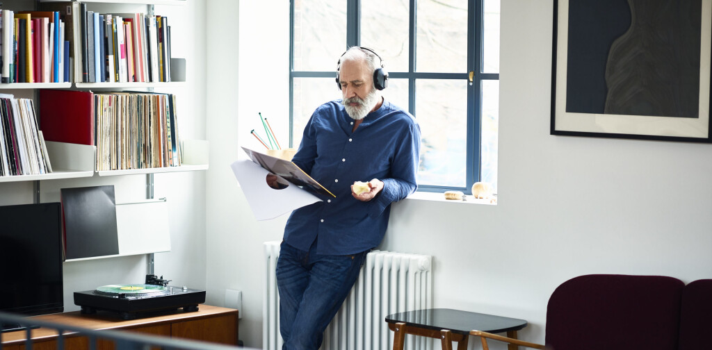 Senior males Hipster wearing headphone, leaning on windowsill, reading album cover, engrossed in music, listening to favourite song, music fan
