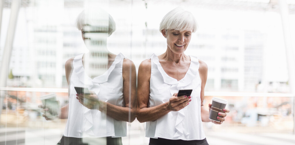 Smiling senior woman with cell phone and takeway coffee outdoors