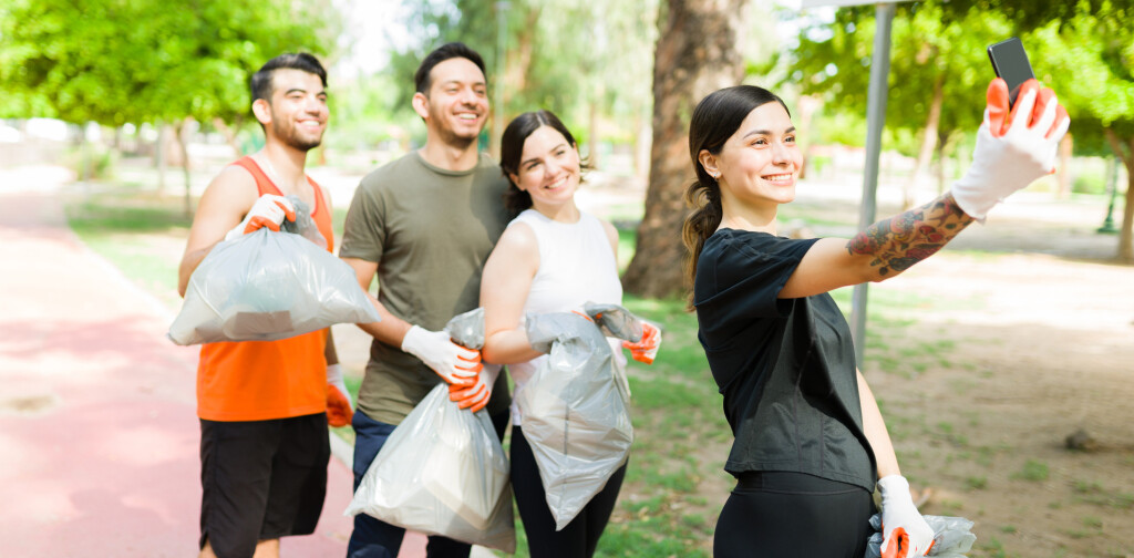 Beautiful young woman and her group of diverse friends taking a selfie with her smartphone after running while picking up trash outdoors