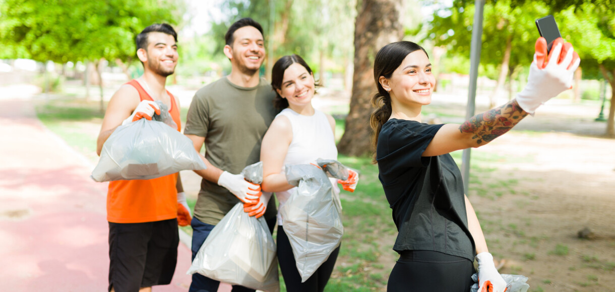 Beautiful young woman and her group of diverse friends taking a selfie with her smartphone after running while picking up trash outdoors