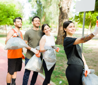 Beautiful young woman and her group of diverse friends taking a selfie with her smartphone after running while picking up trash outdoors